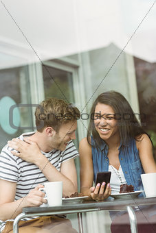 Smiling friends with chocolate cake using smartphone