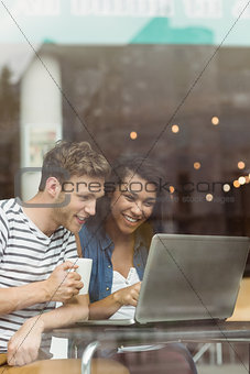 Smiling friends with a hot drink using laptop