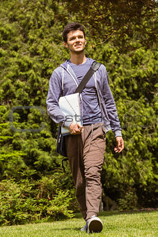 Student walking with shoulder bag and holding notepad