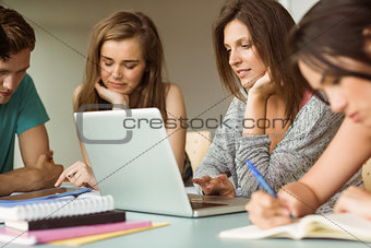 Smiling friends sitting studying and using laptop