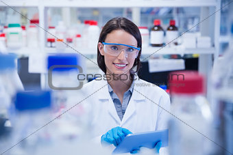 Smiling chemist wearing safety glasses and using tablet pc