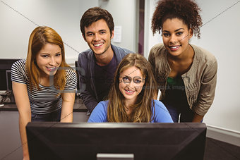 Smiling students using computer together looking at camera