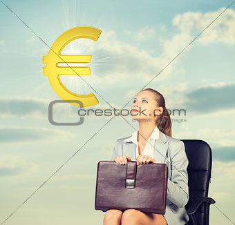 Businesswoman sitting on office chair, looking at euro sign in the air