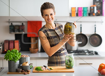 Portrait of happy young housewife showing jar of pickled cucumbe
