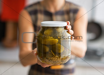 Closeup on young housewife showing jar of pickled cucumbers