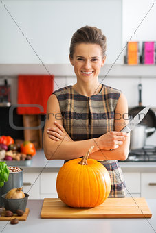 Portrait of happy young housewife with pumpkin in kitchen