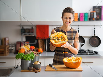 Portrait of happy young housewife in kitchen showing pumpkin