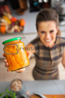 Closeup on happy young housewife showing jar of pickled pumpkin