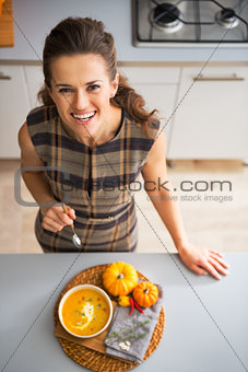Portrait of happy young housewife eating pumpkin soup