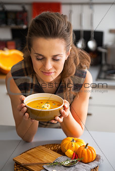 Young woman enjoying pumpkin soup in kitchen