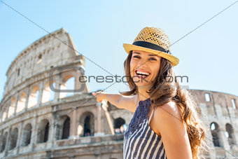 Smiling young woman pointing on colosseum in rome, italy