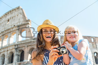 Happy mother and baby girl with photo camera near colosseum in r