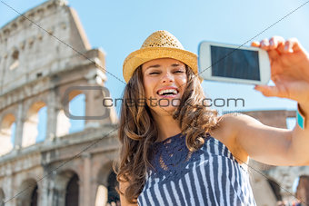 Smiling young woman making selfie in front of colosseum in rome,