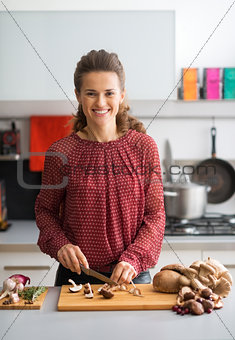 Happy young housewife cutting mushrooms in kitchen