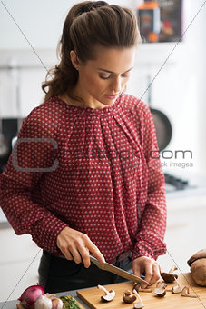 Young housewife cutting mushrooms in kitchen