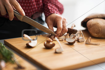 Closeup on young housewife cutting mushrooms in kitchen