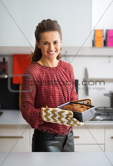 Portrait of happy young housewife with baking dish with bread