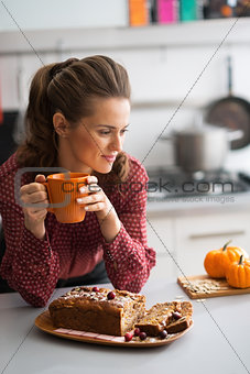 Young housewife drinking tea with freshly baked pumpkin bread wi
