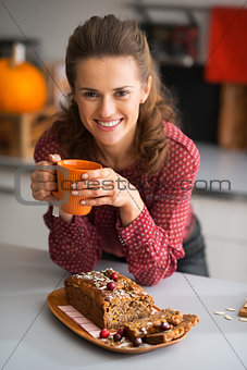 Happy young housewife drinking tea with freshly baked pumpkin br