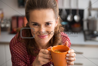 Portrait of happy young housewife drinking tea in kitchen