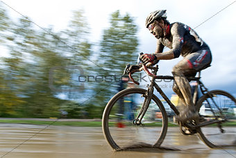 Male cyclist riding through a mud puddle