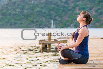 girl with a long braid relaxes in a lotus position on the pier