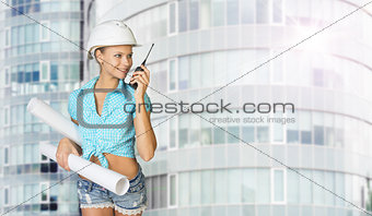 Woman in hard hat holding drawing rolls, talking on walkie talki