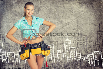 Woman in tool belt standing akimbo against stone wall with sketch of city on it
