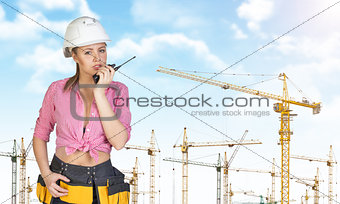 Woman in hard hat and tool belt talking on walkie talkie