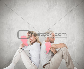 Composite image of unhappy couple sitting holding two halves of broken heart