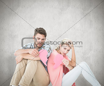 Composite image of attractive young couple sitting holding two halves of broken heart