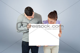 Composite image of young couple holding banner together and looking down