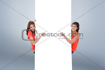 Composite image of teenage girls looking at the camera while pointing their fingers on a blank poste