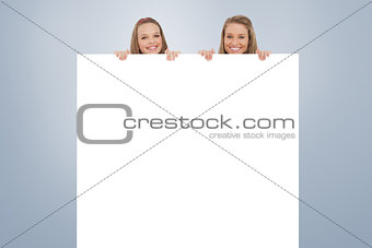Composite image of close up of young women behind a blank sign