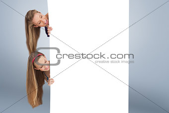 Composite image of close up of two smiling long hair students behind a blank sign