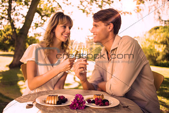 Cute happy couple sitting outside toasting with champagne with dessert