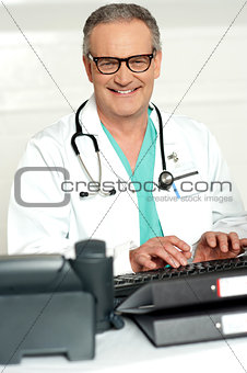 Smiling physician in eye wear typing on keyboard