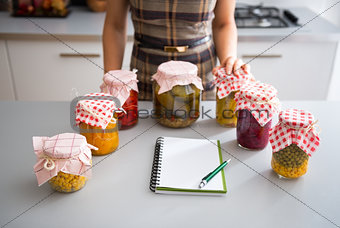 Closeup on notepad and young housewife with jars of pickled vege