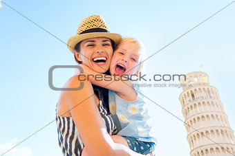Happy mother and baby girl hugging in front of leaning tower of 