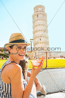 Portrait of happy young woman eating pizza in front of leaning t