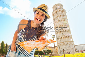 Smiling young woman giving pizza in front of leaning tower of pi