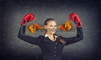 Confident woman in red gloves with fire from ears. Concrete gray wall as backdrop