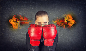 Woman boxing gloves covers her face. Fire from ears. Concrete gray wall as backdrop