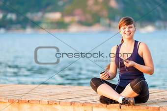 funny and beautiful girl with headphones sitting on the pier in 