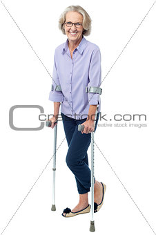 Bespectacled old woman walking with crutches