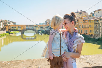 Happy mother and baby girl hugging on bridge overlooking ponte v