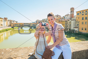 Mother and baby girl taking photo while standing on bridge overl