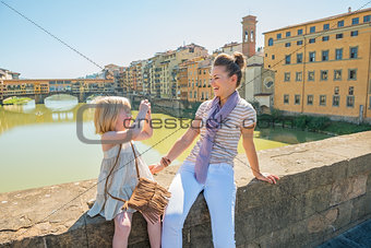 Baby girl taking photo of mother while sitting on bridge overloo