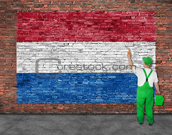 House painter paints flag of Hetherlands on brick wall