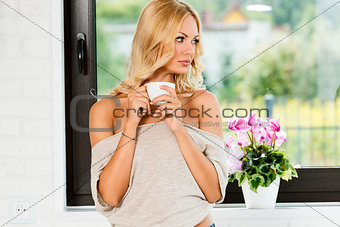 woman looking out window with hot coffee 